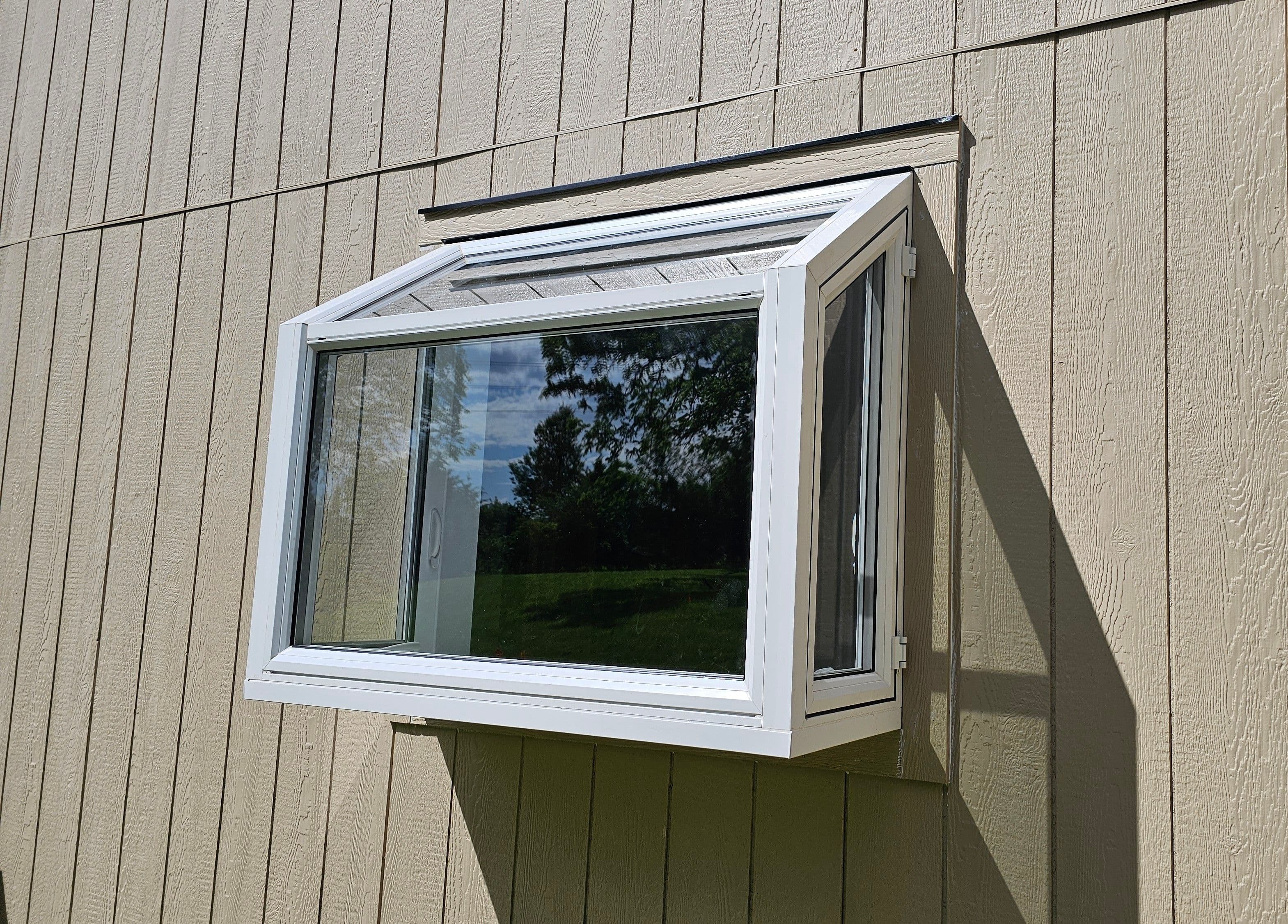White projecting garden or bay-style replacement window set into vertical siding.