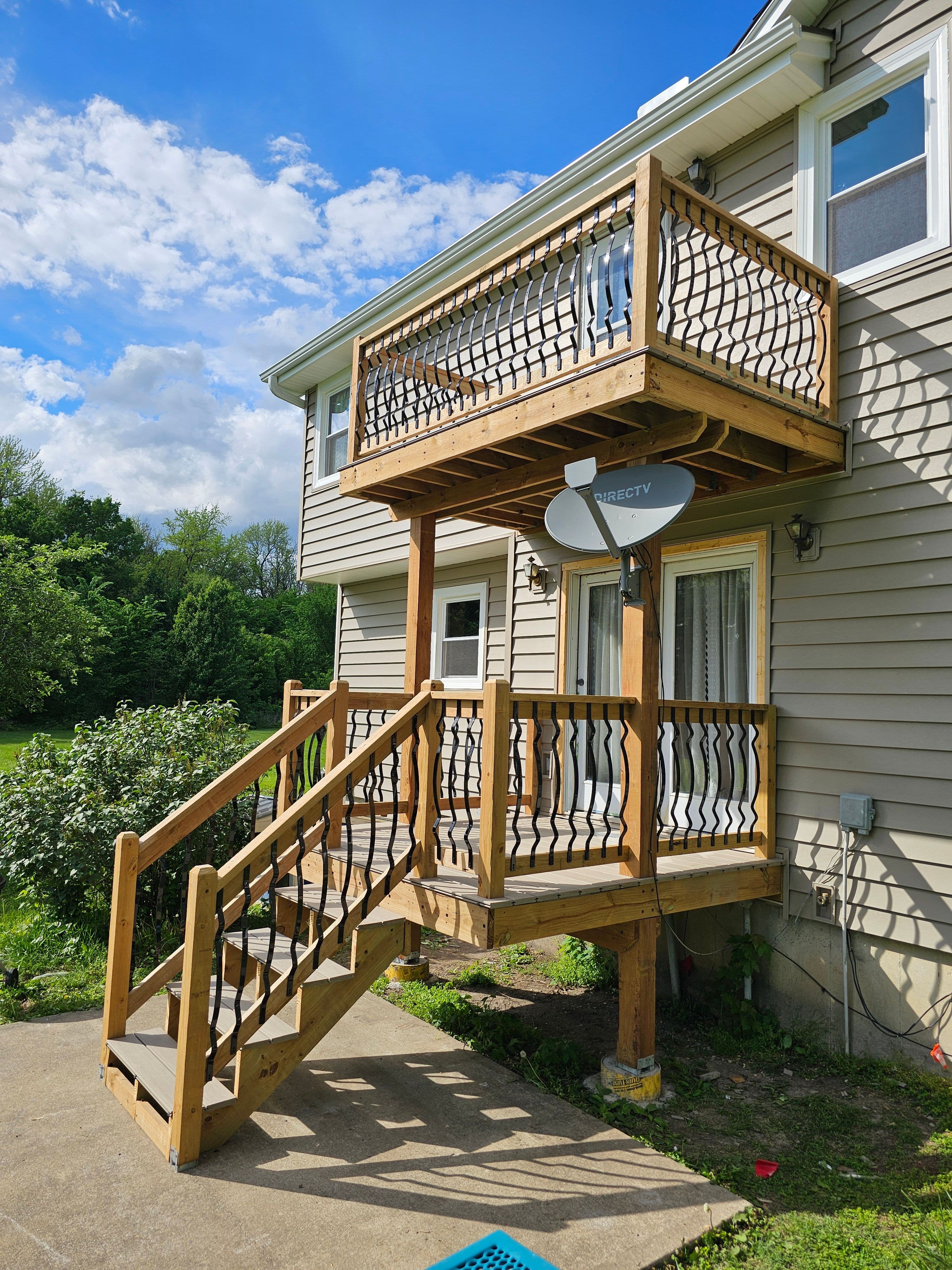Exterior two-level wood deck and stairs with black metal balusters on residential siding.