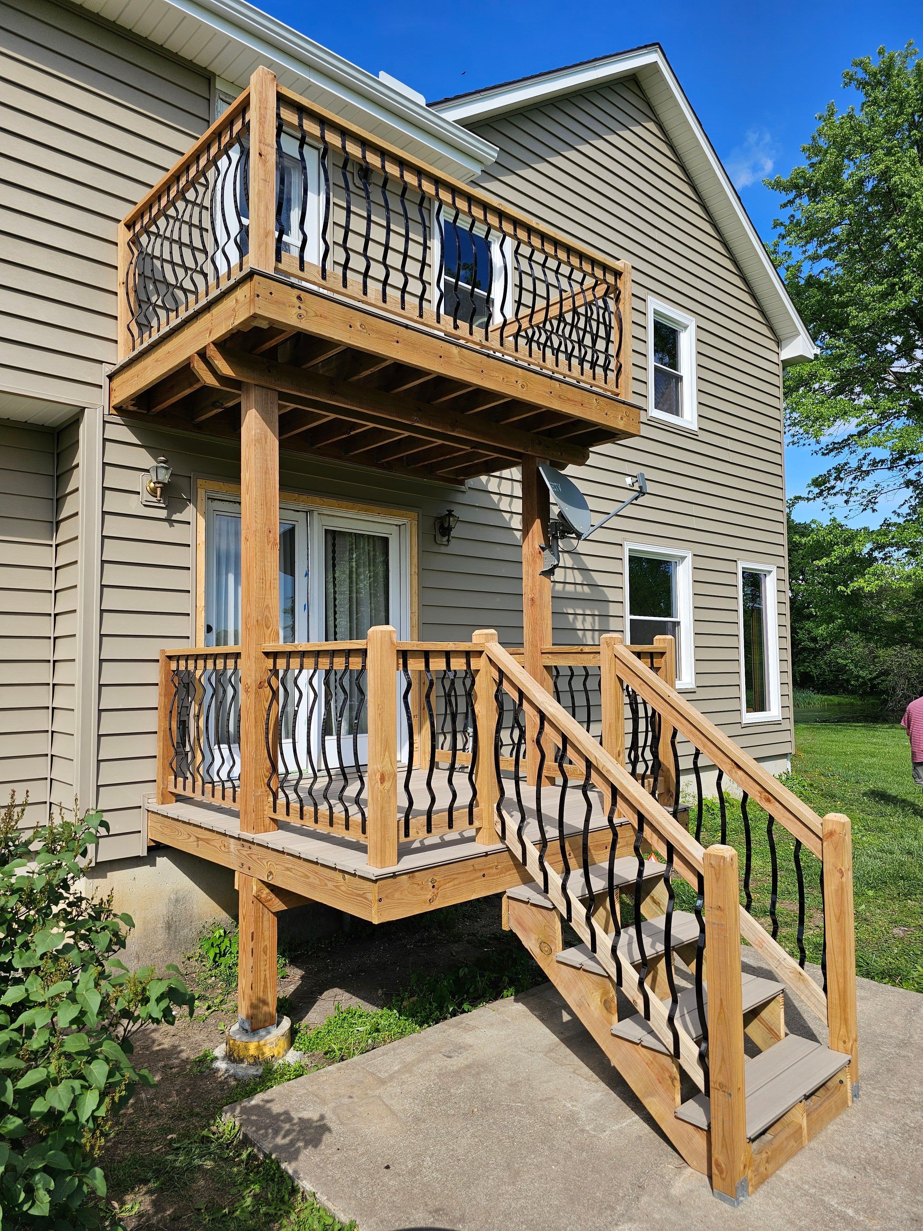 Exterior two-level wood deck and stairs with black metal balusters on residential siding.