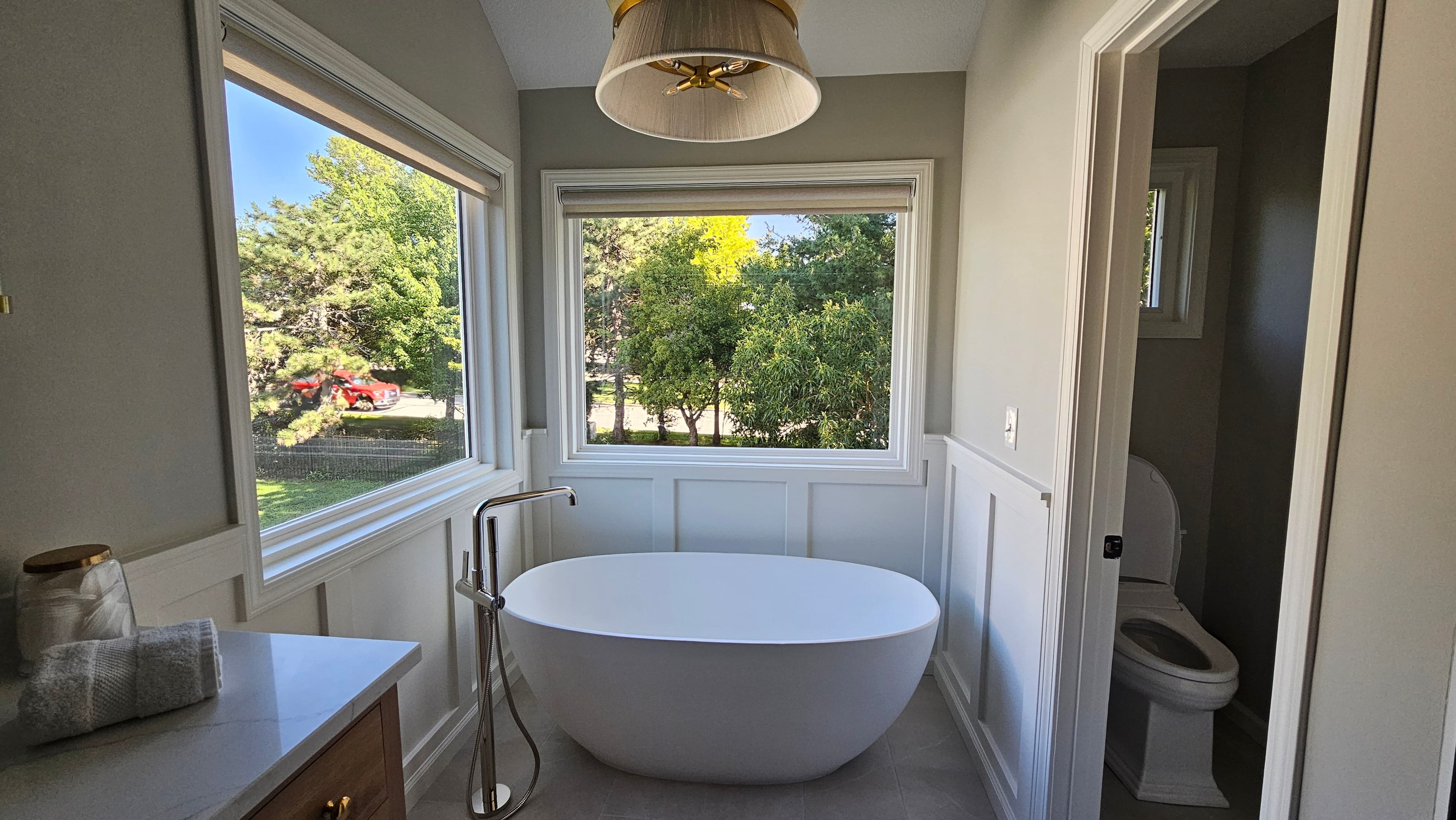 Remodeled bathroom with freestanding tub, large windows, wainscoting, vanity, and separate toilet room.